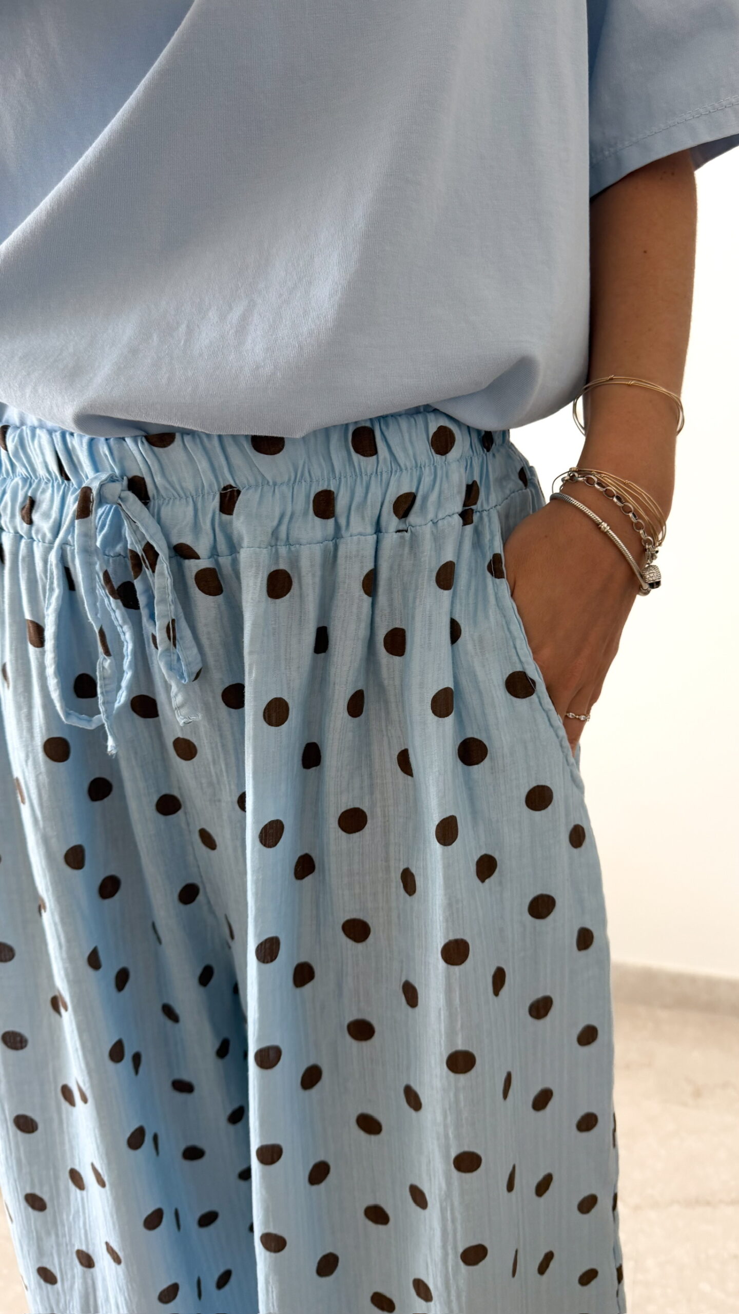 Femme portant un pantalon bleu ciel à pois marron avec taille élastique et lien de serrage, associé à un haut uni.