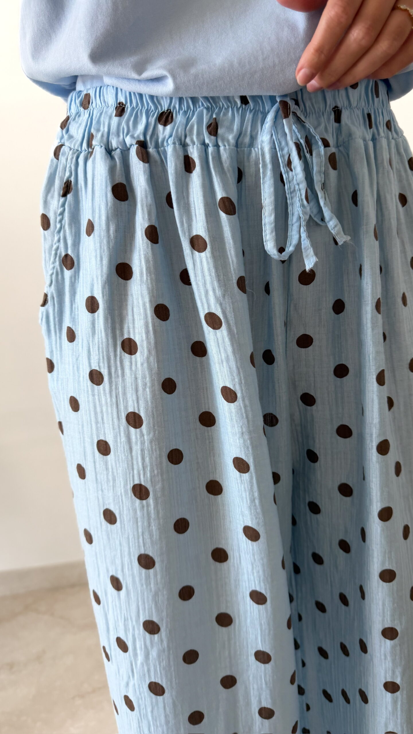 Femme portant un pantalon bleu ciel à pois marron avec taille élastique et lien de serrage, associé à un haut uni.
