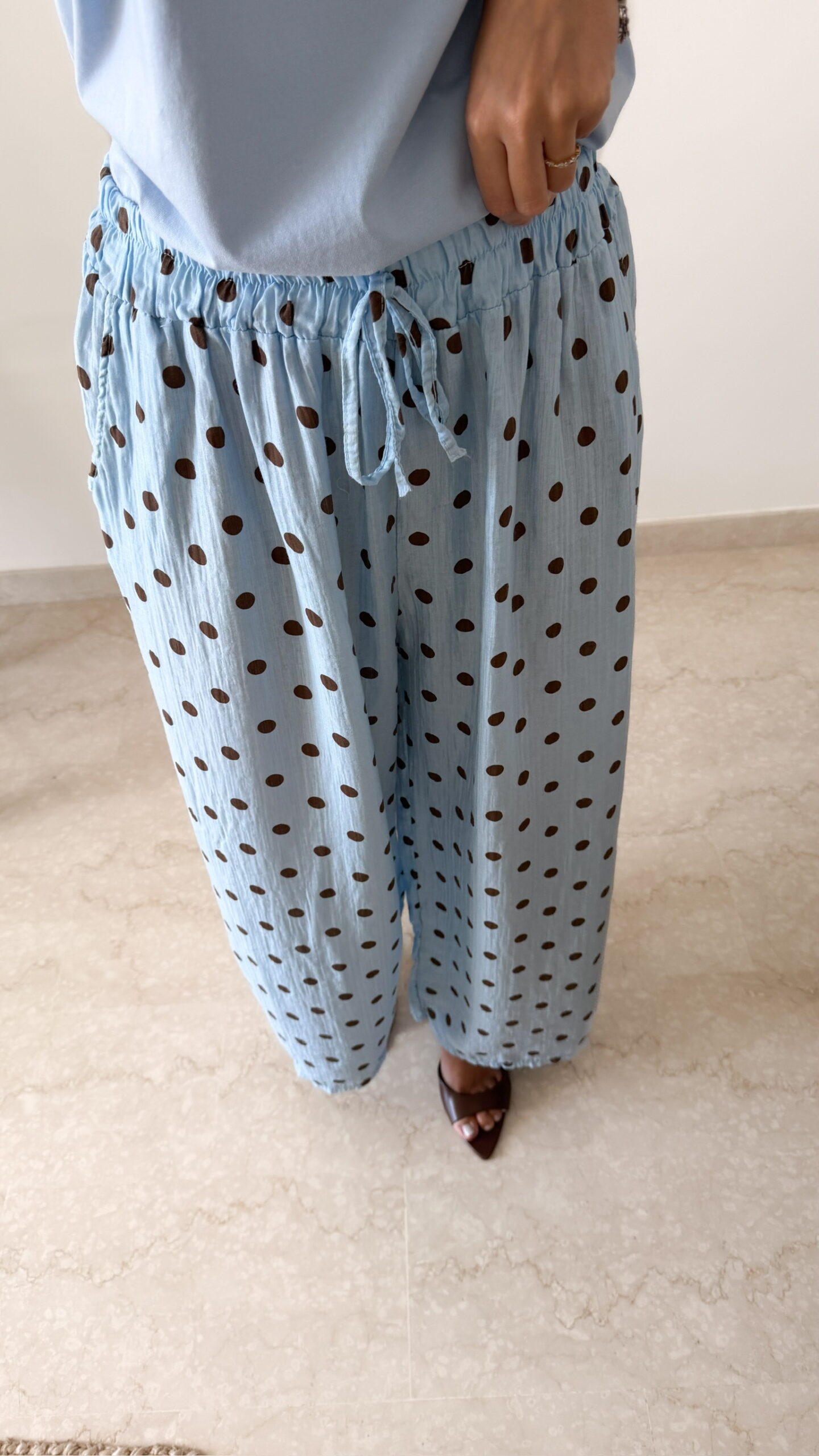 Femme portant un pantalon bleu ciel à pois marron avec taille élastique et lien de serrage, associé à un haut uni.