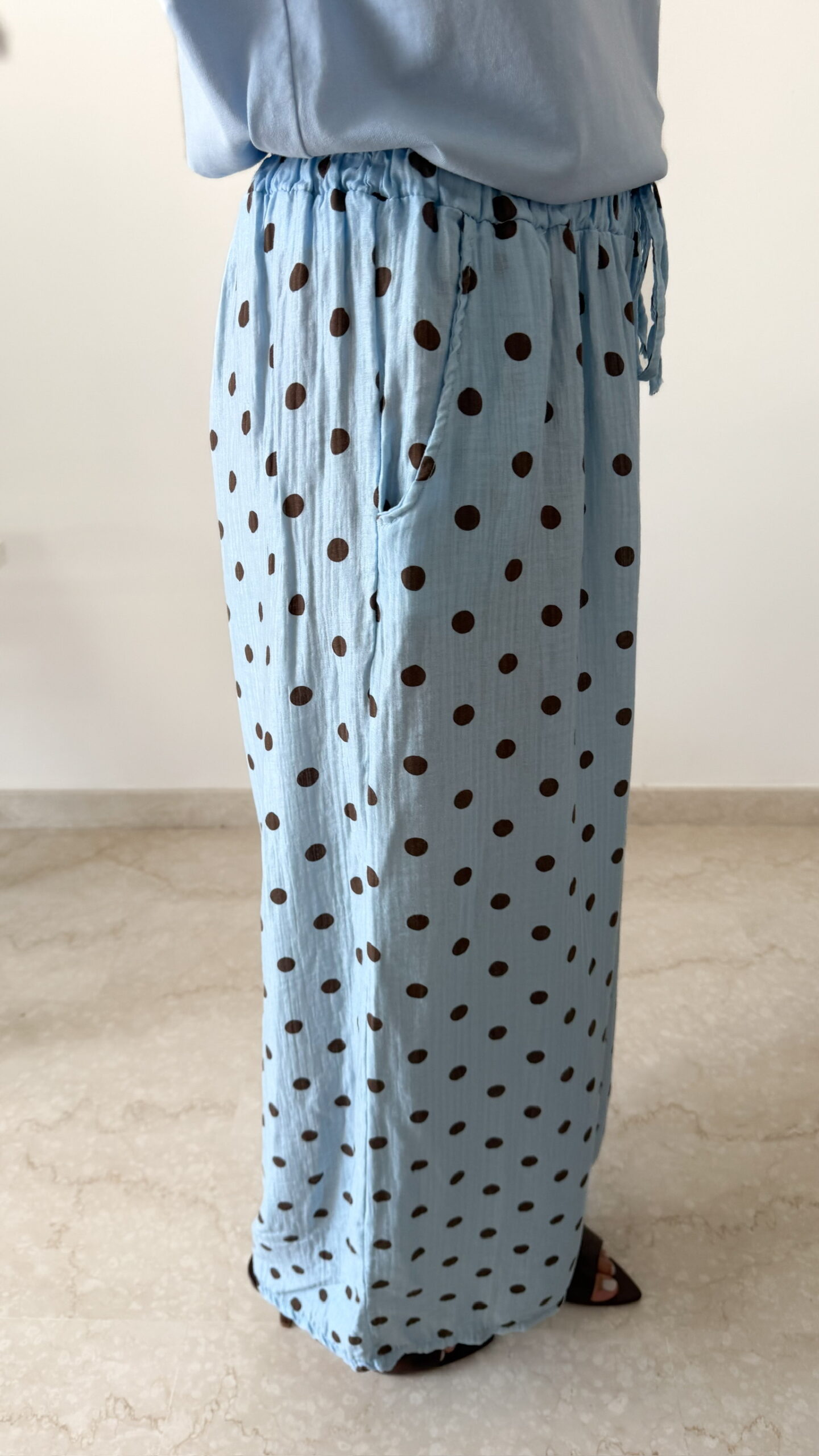 Femme portant un pantalon bleu ciel à pois marron avec taille élastique et lien de serrage, associé à un haut uni.