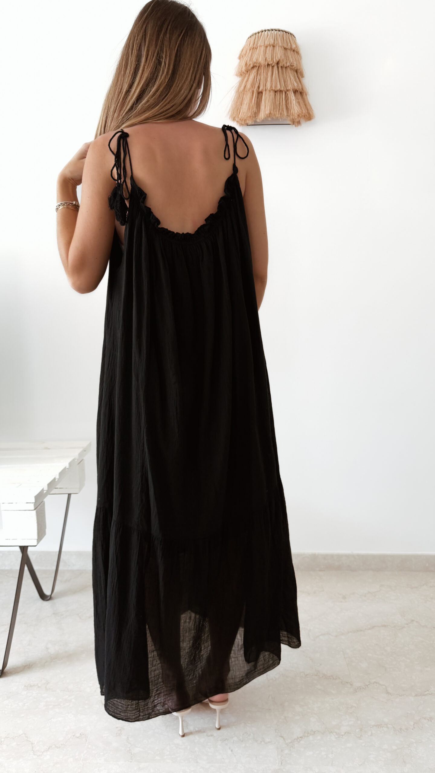 Robe longue noire à fines bretelles pour femme, coupe ample et fluide avec détails pompons, style bohème chic.