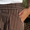 Pantalon fluide marron à rayures verticales blanches, taille haute et coupe large, porté avec un débardeur blanc.