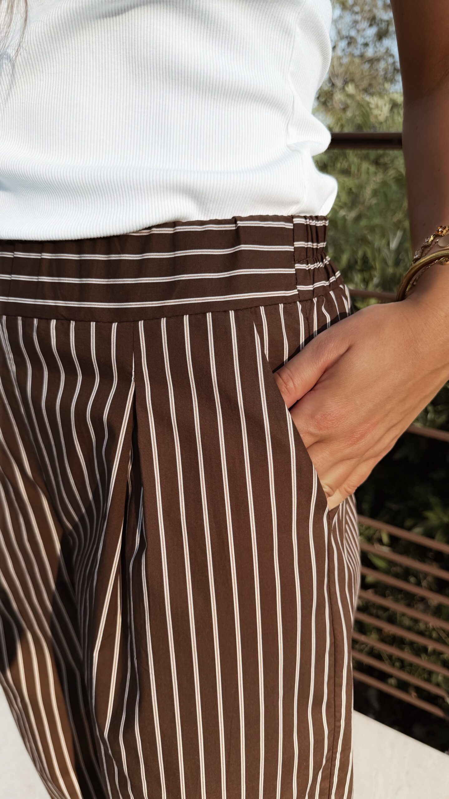 Pantalon fluide marron à rayures verticales blanches, taille haute et coupe large, porté avec un débardeur blanc.