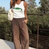 Pantalon fluide marron à rayures verticales blanches, taille haute et coupe large, porté avec un débardeur blanc.