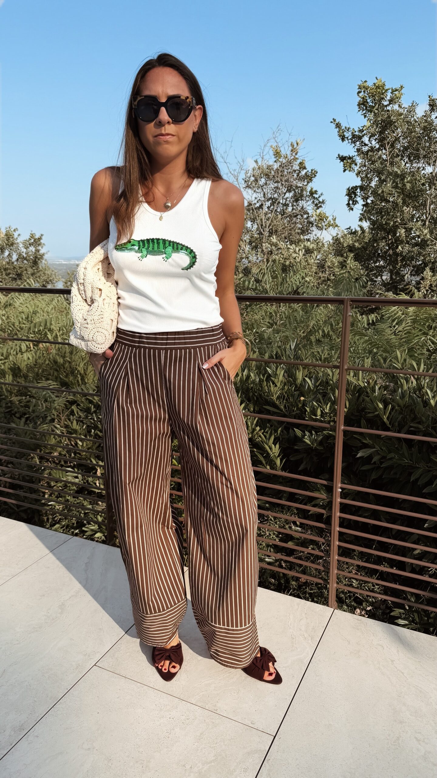 Pantalon fluide marron à rayures verticales blanches, taille haute et coupe large, porté avec un débardeur blanc.
