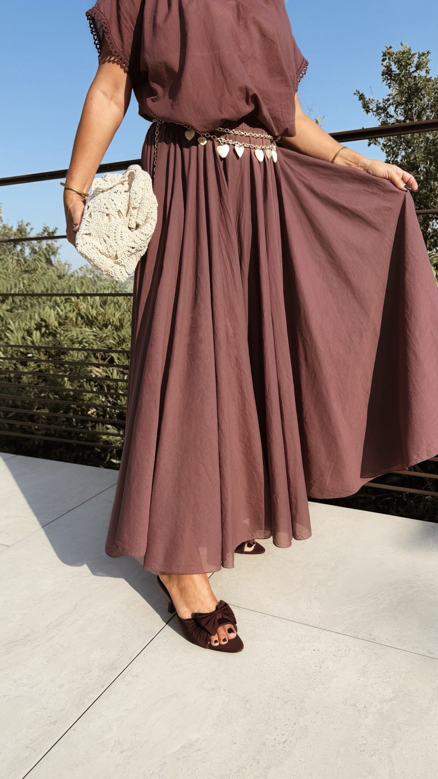 Ensemble bordeaux composé d'une blouse fluide à manches courtes et d'une jupe longue évasée, porté avec une pochette en crochet écru.