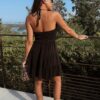 Robe courte noire à fines bretelles avec décolleté drapé, portée avec des mules à talon bordeaux et une pochette imprimé léopard.