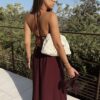 Robe longue dos nu bordeaux à fines bretelles, décolleté plongeant et fente sur la jambe, portée avec des mules à talon assorties.