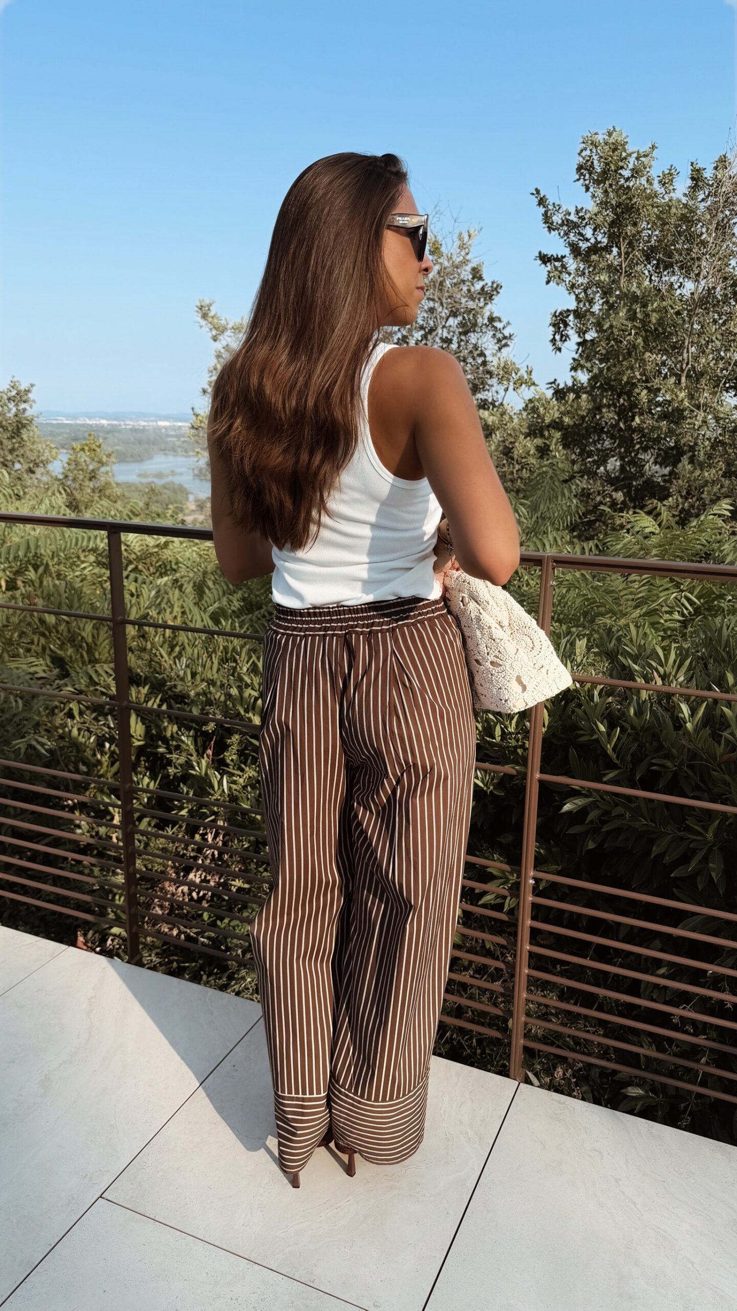 Pantalon fluide marron à rayures verticales blanches, taille haute et coupe large, porté avec un débardeur blanc.