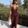 Robe longue dos nu bordeaux à fines bretelles, décolleté plongeant et fente sur la jambe, portée avec des mules à talon assorties.