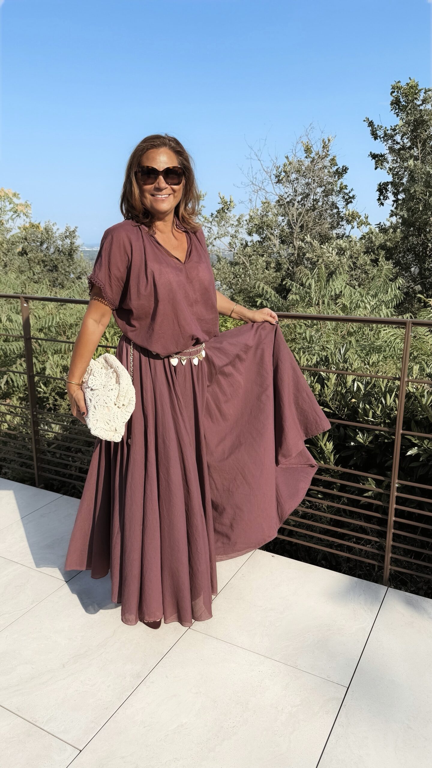 Ensemble bordeaux composé d'une blouse fluide à manches courtes et d'une jupe longue évasée, porté avec une pochette en crochet écru.