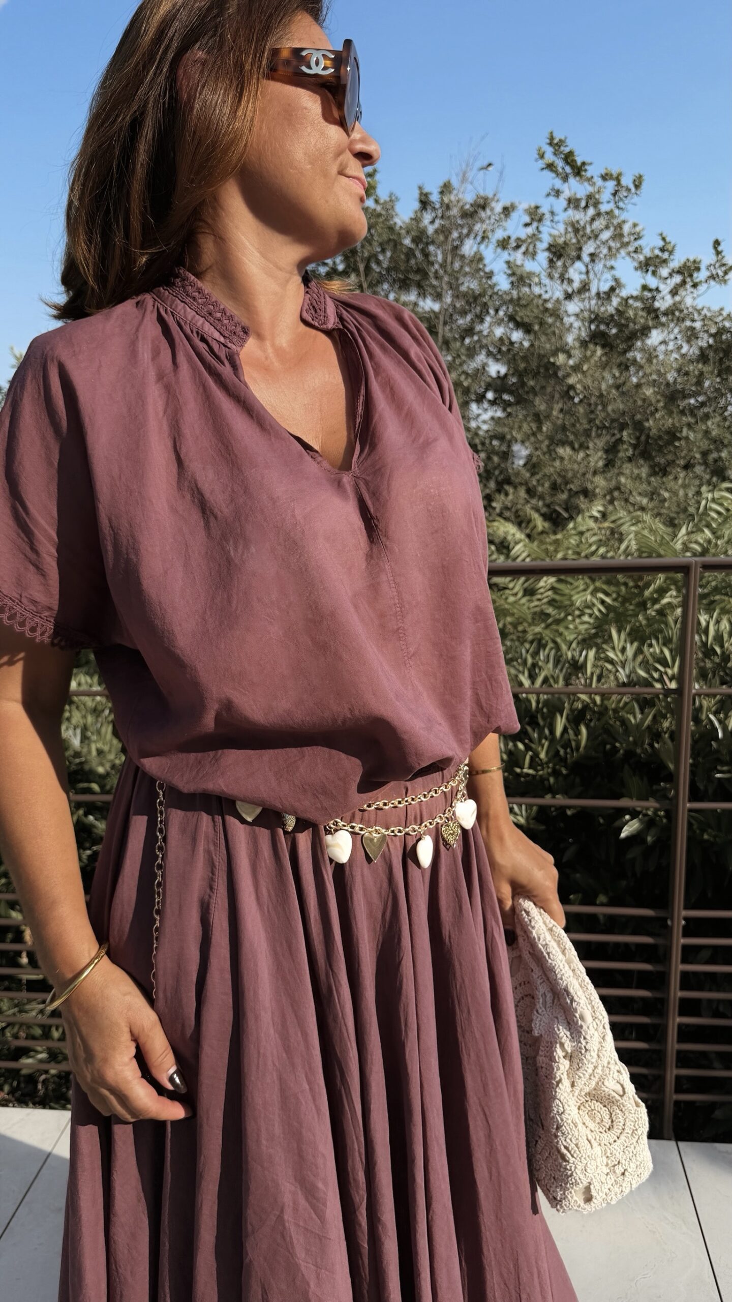 Ensemble bordeaux composé d'une blouse fluide à manches courtes et d'une jupe longue évasée, porté avec une pochette en crochet écru.