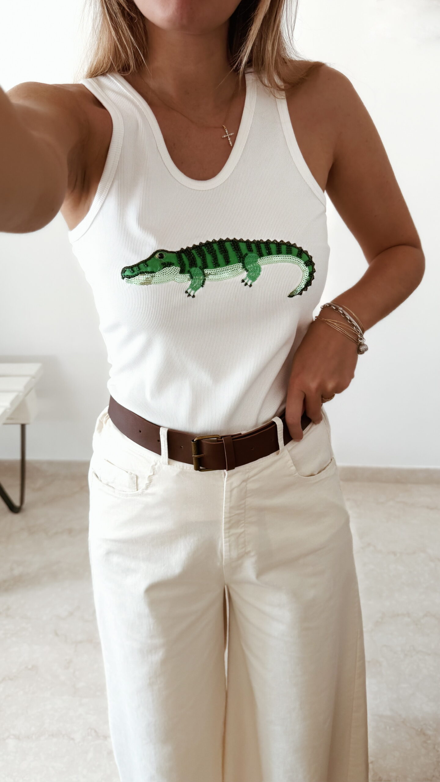 Débardeur femme blanc côtelé avec motif crocodile vert brodé en sequins, porté avec un pantalon écru taille haute pour un look estival tendance.