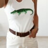 Débardeur femme blanc côtelé avec motif crocodile vert brodé en sequins, porté avec un pantalon écru taille haute pour un look estival tendance.