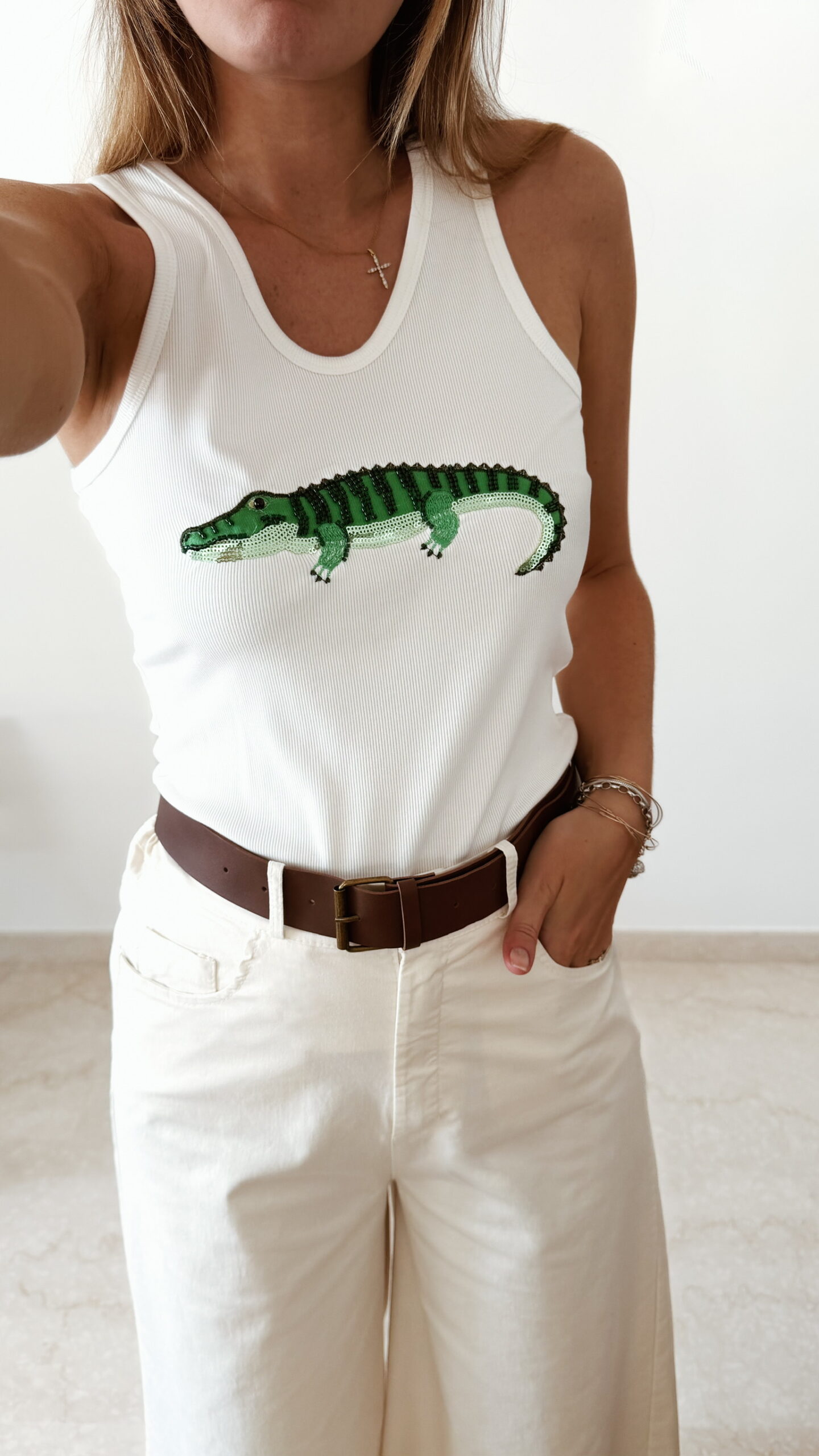 Débardeur femme blanc côtelé avec motif crocodile vert brodé en sequins, porté avec un pantalon écru taille haute pour un look estival tendance.