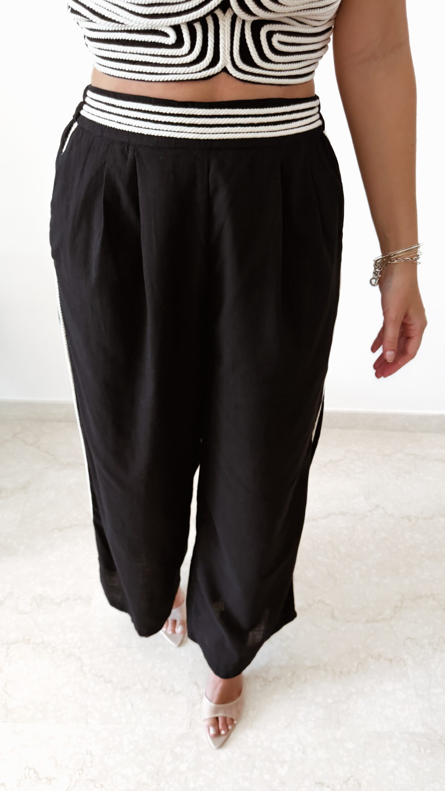 Ensemble femme noir composé d'un top texturé blanc et noir à bretelles et d'un pantalon fluide taille haute, style chic et élégant.
