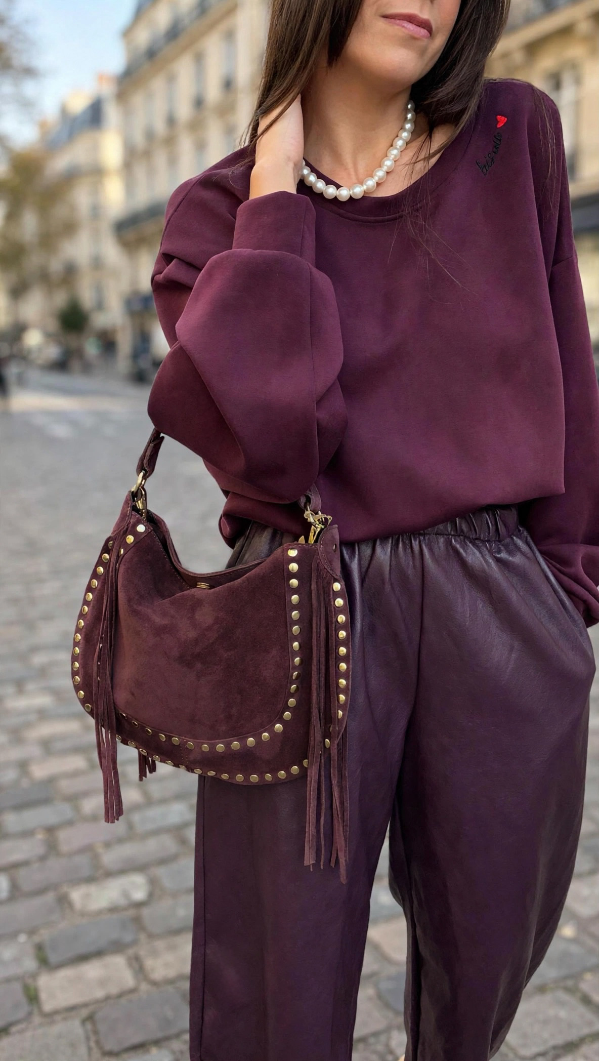 Femme portant un sweat bordeaux et un pantalon large en simili cuir bordeaux avec sac à main bordeaux clouté à franges