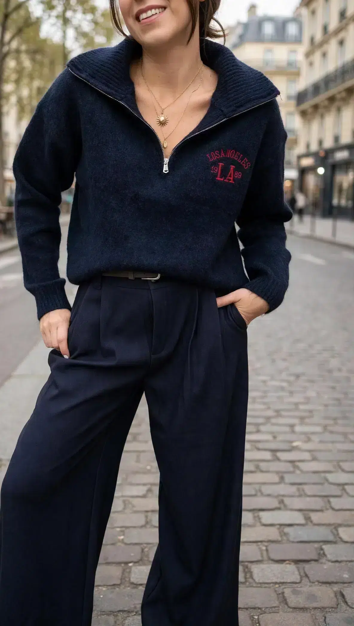 Pull femme bleu marine Los Angeles à col montant zippé avec inscription rouge sur la poitrine, porté avec un pantalon large bleu marine.
