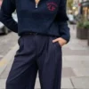 Pull femme bleu marine Los Angeles à col montant zippé avec inscription rouge sur la poitrine, porté avec un pantalon large bleu marine.