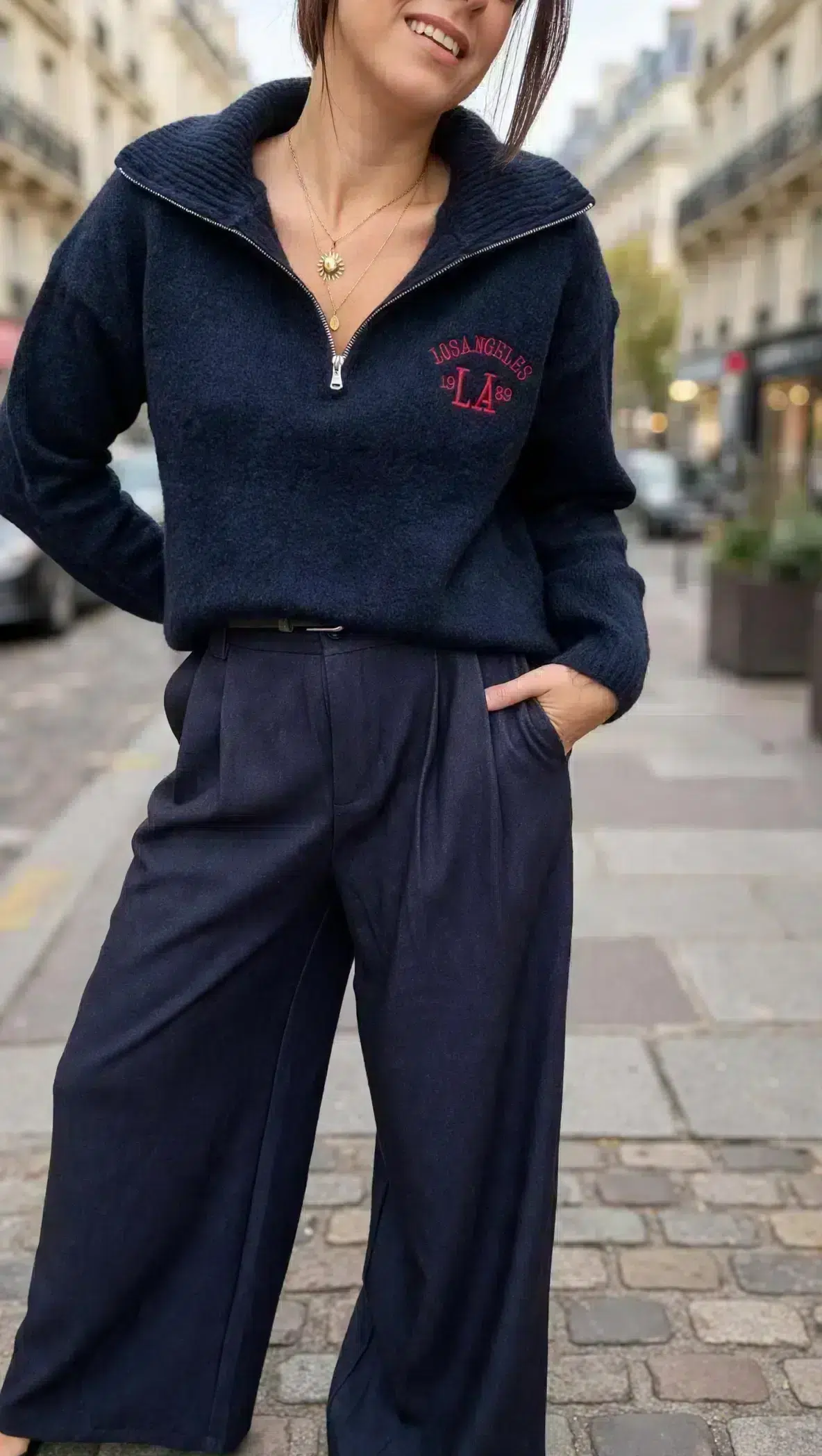 Pull femme bleu marine Los Angeles à col montant zippé avec inscription rouge sur la poitrine, porté avec un pantalon large bleu marine.