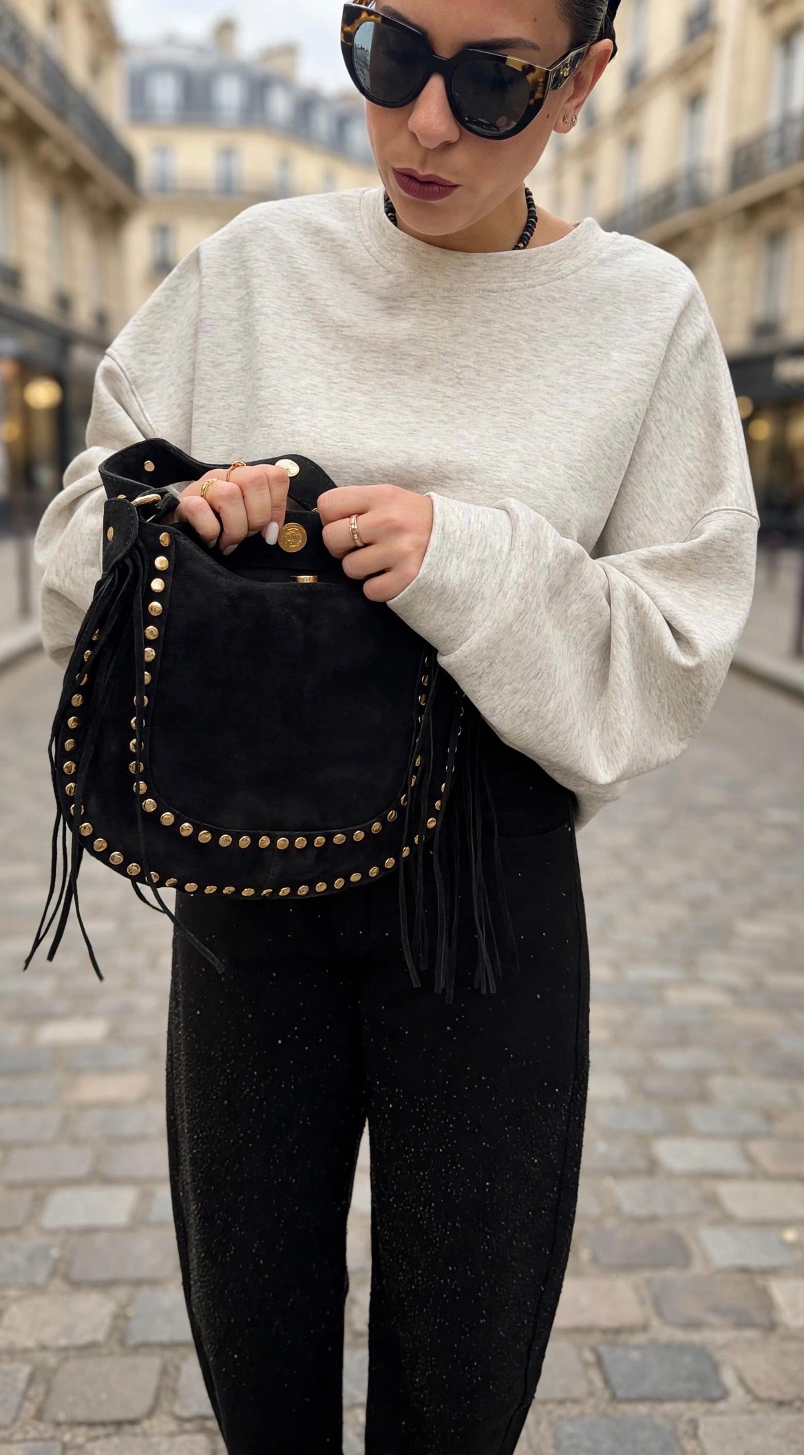 Sac à main femme noir clouté à franges porté avec un sweatshirt gris et un pantalon noir